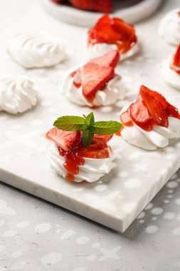 Taze çilek ve kırmızı reçelli mini pavlova. Mermer tahtada, beyaz arka planda lezzetli kremalı pastalar.