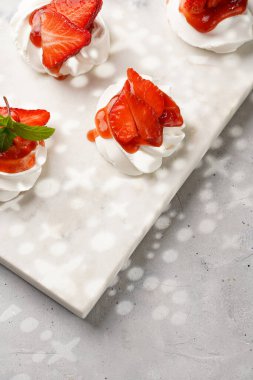 Taze çilek ve kırmızı reçelli mini pavlova. Mermer tahtada, beyaz arka planda lezzetli kremalı pastalar.