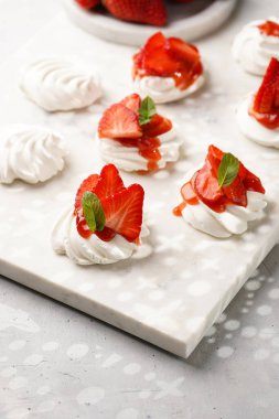 Taze çilek ve kırmızı reçelli mini pavlova. Mermer tahtada, beyaz arka planda lezzetli kremalı pastalar.