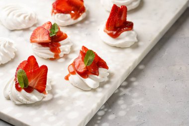 Taze çilek ve kırmızı reçelli mini pavlova. Mermer tahtada, beyaz arka planda lezzetli kremalı pastalar.