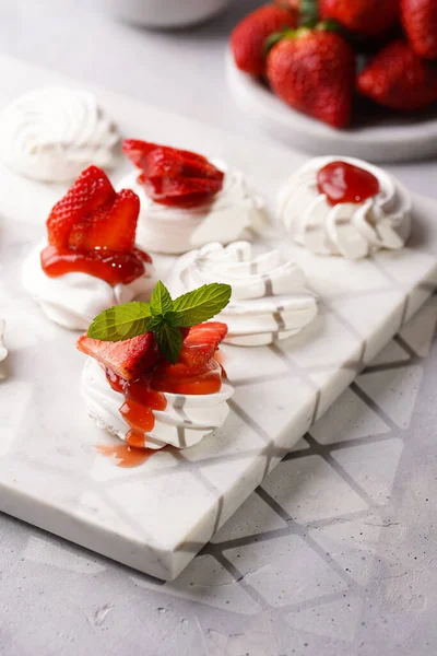 Taze çilek ve kırmızı reçelli mini pavlova. Mermer tahtada, beyaz arka planda lezzetli kremalı pastalar.