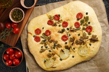 Çiçek boyama Focaccia, İtalyan bahçe düz ekmek sanatı maydanozlu, domatesli, soğanlı, susam tohumlu ve kapari siyah yapılı arka planda.