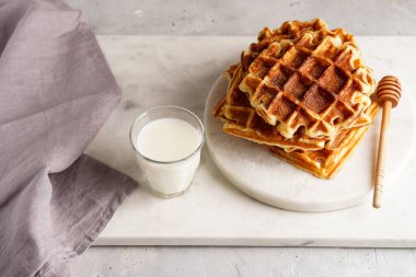 Tatlı kahvaltı - ballı ev yapımı Belçika waffleları ve beyaz yuvarlak mermer tahtaya istiflenmiş toz şeker ve sütlü küçük bardak