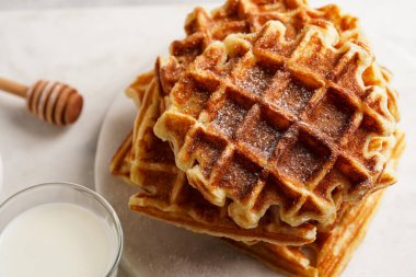 Tatlı kahvaltı - ballı ev yapımı Belçika waffleları ve beyaz yuvarlak mermer tahtaya istiflenmiş toz şeker ve sütlü küçük bardak