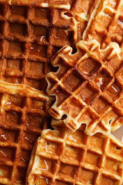 Fresh homemade sweet belgian waffles with honey and powdered sugar filling the frame