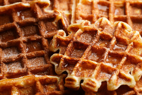 Fresh homemade sweet belgian waffles with honey and powdered sugar filling the frame
