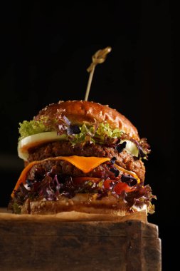 Duble angus biftekli hamburger, domates, marul, peynir ve barbekü soslu ahşap tahta üzerinde, koyu arkaplan