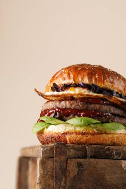 Duble angus bifteği köfteli hamburger, domates, ıspanak, sahanda yumurta ve barbekü soslu ahşap tahta, pastel arka plan, metin için kopyalama alanı