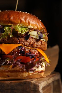 Duble angus biftekli hamburger, domates, marul, peynir ve barbekü soslu ahşap tahta üzerinde, koyu arkaplan