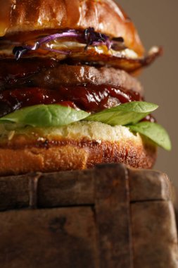 Duble angus bifteği köfteli hamburger, domates, ıspanak, sahanda yumurta ve barbekü sosu ahşap tahtada, pastel arka plan, yakın plan.