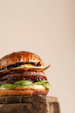 Duble angus bifteği köfteli hamburger, domates, ıspanak, kızarmış yumurta ve barbekü sosu ahşap tahtada, pastel arka planda.