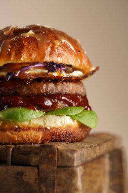 Duble angus bifteği köfteli hamburger, domates, ıspanak, kızarmış yumurta ve barbekü sosu ahşap tahtada, pastel arka planda.