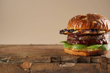 Çift angus biftekli hamburger, domates, ıspanak, sahanda yumurta ve barbekü soslu ahşap tahta, pastel arka plan, kopyalama alanı.