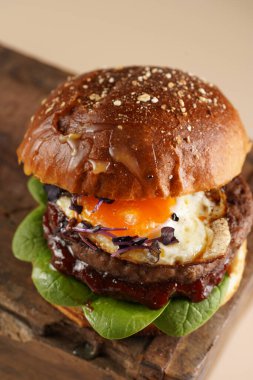 Duble angus bifteği köfteli hamburger, domates, ıspanak, kızarmış yumurta ve barbekü sosu ahşap tahtada, pastel arka planda.