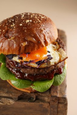 Duble angus bifteği köfteli hamburger, domates, ıspanak, kızarmış yumurta ve barbekü sosu ahşap tahtada, pastel arka planda.