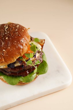 Çift angus biftekli hamburger, domates, ıspanak, kızarmış yumurta ve barbekü sosu mermer tahtada, pastel arka planda.