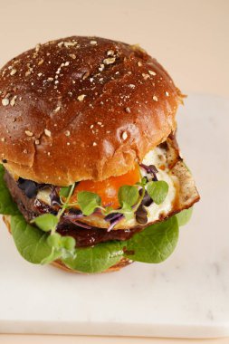 Çift angus biftekli hamburger, domates, ıspanak, kızarmış yumurta ve barbekü sosu mermer tahtada, pastel arka planda.