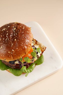 Çift angus biftekli hamburger, domates, ıspanak, kızarmış yumurta ve barbekü sosu mermer tahtada, pastel arka planda.