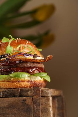 Duble angus bifteği köfteli hamburger, domates, ıspanak, kızarmış yumurta ve barbekü sosu ahşap tahtada, pastel arka planda.