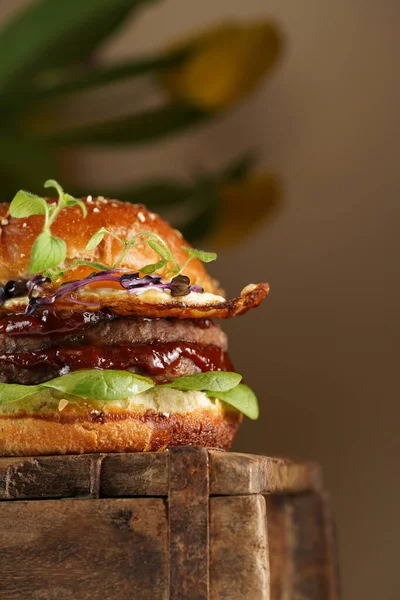 Duble angus bifteği köfteli hamburger, domates, ıspanak, kızarmış yumurta ve barbekü sosu ahşap tahtada, pastel arka planda.