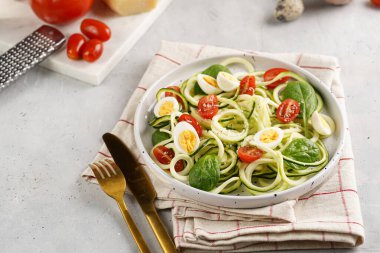 Keto paleo düşük karbonhidratlı makarna: parmesan peynirli kabaklı şehriye, kiraz domatesli bıldırcın yumurtası ve mutfak havlusu açık gri yüzey.
