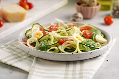 Keto paleo düşük karbonhidratlı makarna: parmesan peynirli kabaklı şehriye, kiraz domatesli bıldırcın yumurtası ve mutfak havlusu açık gri yüzey.