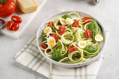 Keto paleo düşük karbonhidratlı makarna: parmesan peynirli kabaklı şehriye, kiraz domatesli bıldırcın yumurtası ve mutfak havlusu açık gri yüzey.