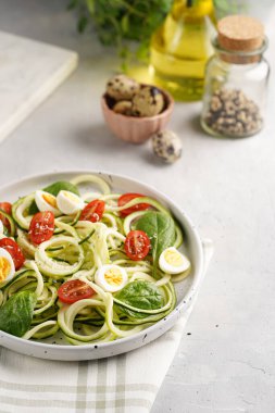 Keto paleo düşük karbonhidratlı makarna: parmesan peynirli kabaklı şehriye, kiraz domatesli bıldırcın yumurtası ve mutfak havlusu açık gri yüzey.