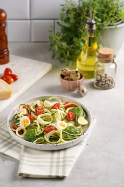 Keto paleo düşük karbonhidratlı makarna: parmesan peynirli kabaklı şehriye, kiraz domatesli bıldırcın yumurtası ve mutfak havlusu açık gri yüzey.