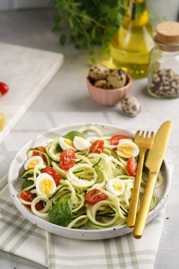 Keto paleo düşük karbonhidratlı makarna: parmesan peynirli kabaklı şehriye, kiraz domatesli bıldırcın yumurtası ve mutfak havlusu açık gri yüzey.