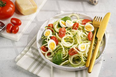 Keto paleo düşük karbonhidratlı makarna: parmesan peynirli kabaklı şehriye, kiraz domatesli bıldırcın yumurtası ve mutfak havlusu açık gri yüzey.