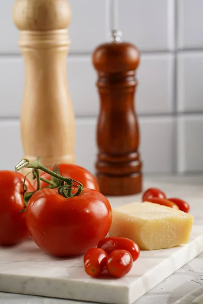 Ingredients for cooking: big tomatoes, small cherry tomatoes, parmesan cheese, oregano herb, salt and pepper mills on marble board