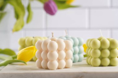 Many bubble candles - off-white, beige-colored and blue - on marble board with spring flowers - yellow and purple tulips clipart