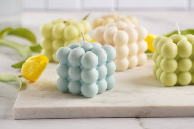 Bahar çiçekleriyle mermer tahtada beyaz, bej renkli ve mavi renkli birçok baloncuk mumu bulunur. Sarı ve mor laleler.