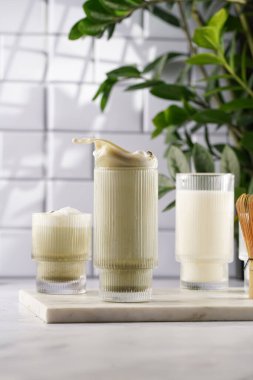 Japon yeşil çay tozu ve beyaz mutfaktaki mermer tahtada çırpılmış süt.