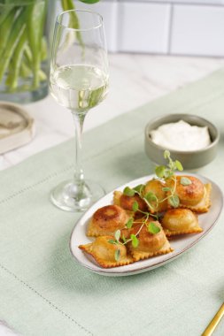 Bol yağda kızartılmış geleneksel İtalyan yemeği - ravioli, kıymalı börek, kekik dalı, ekşi krema, yeşil masa örtüsünde şampanya.