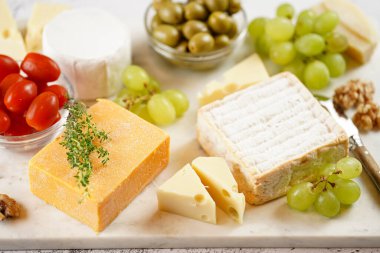 Organik peynirli peynir tabağı - mavi peynirli çedar, emmantaler, güçlü kokulu Fransız yumuşak peyniri, İtalyan parmesan peyniri, üzümler, domates, zeytin, fındık ve mermer tahtada kraker