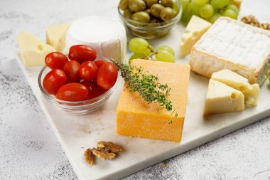 Organik peynirli peynir tabağı - mavi peynirli çedar, emmantaler, güçlü kokulu Fransız yumuşak peyniri, İtalyan parmesan peyniri, üzümler, domates, zeytin, fındık ve mermer tahtada kraker