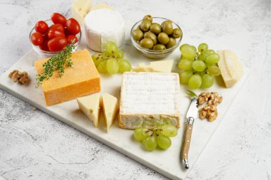 Organik peynirli peynir tabağı - mavi peynirli çedar, emmantaler, güçlü kokulu Fransız yumuşak peyniri, İtalyan parmesan peyniri, üzümler, domates, zeytin, fındık ve mermer tahtada kraker