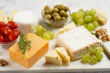 Organik peynirli peynir tabağı - mavi peynirli çedar, emmantaler, güçlü kokulu Fransız yumuşak peyniri, İtalyan parmesan peyniri, üzümler, domates, zeytin, fındık ve mermer tahtada kraker