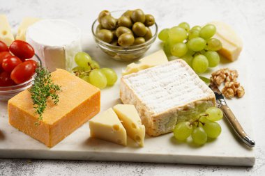 Organik peynirli peynir tabağı - mavi peynirli çedar, emmantaler, güçlü kokulu Fransız yumuşak peyniri, İtalyan parmesan peyniri, üzümler, domates, zeytin, fındık ve mermer tahtada kraker