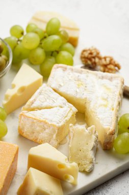 Organik peynirli peynir tabağı - mavi peynirli çedar, emmantaler, güçlü kokulu Fransız yumuşak peyniri, İtalyan parmesan peyniri, üzümler, domates, zeytin, fındık ve mermer tahtada kraker
