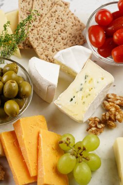 Organik peynirli peynir tabağı - mavi peynirli çedar, emmantaler, güçlü kokulu Fransız yumuşak peyniri, İtalyan parmesan peyniri, üzümler, domates, zeytin, fındık ve mermer tahtada kraker