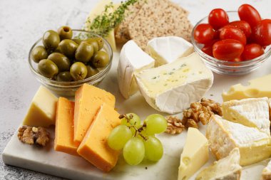 Organik peynirli peynir tabağı - mavi peynirli çedar, emmantaler, güçlü kokulu Fransız yumuşak peyniri, İtalyan parmesan peyniri, üzümler, domates, zeytin, fındık ve mermer tahtada kraker
