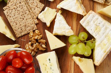 Organik peynirli peynir tabağı - mavi peynirli çedar, emmantaler, güçlü kokulu Fransız yumuşak peyniri, İtalyan parmesan peyniri, üzümler, domates, zeytin, fındık ve tahta üzerinde krakerler