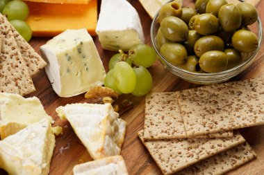 Organik peynirli peynir tabağı - mavi peynirli çedar, emmantaler, güçlü kokulu Fransız yumuşak peyniri, İtalyan parmesan peyniri, üzümler, domates, zeytin, fındık ve tahta üzerinde krakerler