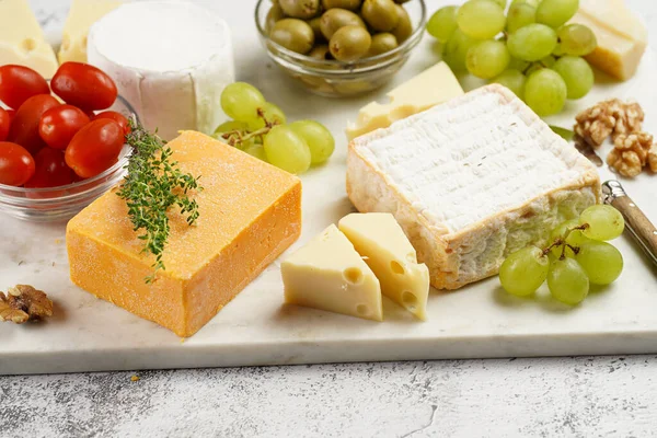 Cheese platter with organic cheeses - blue cheese cheddar, emmantaler, french soft cheese with strong smell, italian parmesan, grapes, tomatoes, olives, nuts and crackers on marble board