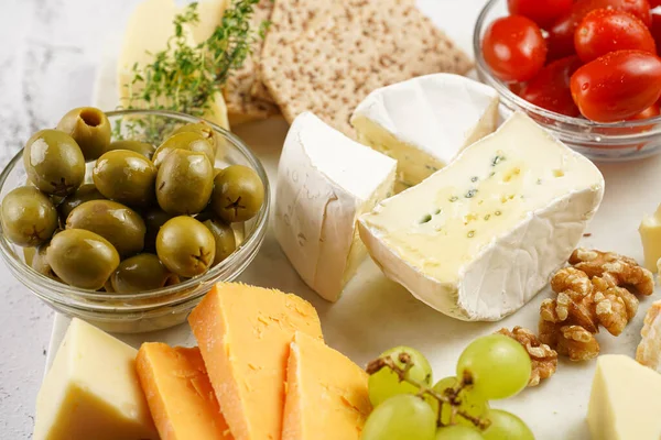 Cheese platter with organic cheeses - blue cheese cheddar, emmantaler, french soft cheese with strong smell, italian parmesan, grapes, tomatoes, olives, nuts and crackers on marble board