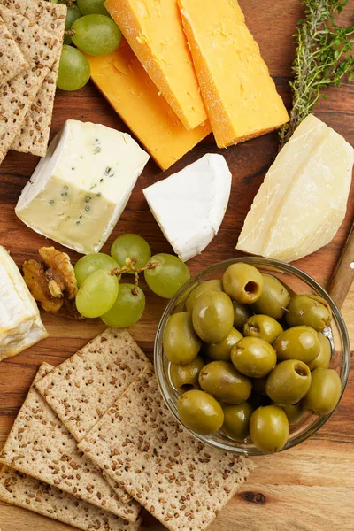 Cheese platter with organic cheeses - blue cheese cheddar, emmantaler, french soft cheese with strong smell, italian parmesan, grapes, tomatoes, olives, nuts and crackers on wooden board