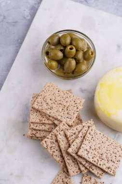 Sağlıklı çıtır çıtır krakerler susam tohumlu, yeşil zeytinli ve mermer tahtada yuvarlak peynirli kaş kaval.